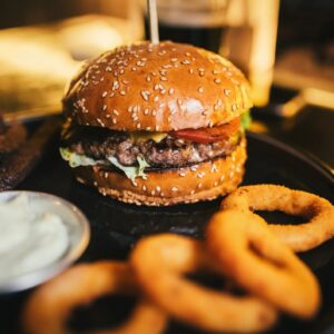 Tasty beef burger with lettuce, cheese and tomato, onion rings and garlic sauce